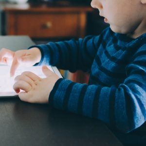 boy sitting on chair beside table using tablet computer